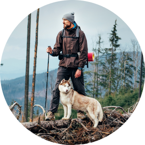 Man dressed for the cold hiking in the mountains with a white and gray dog.
